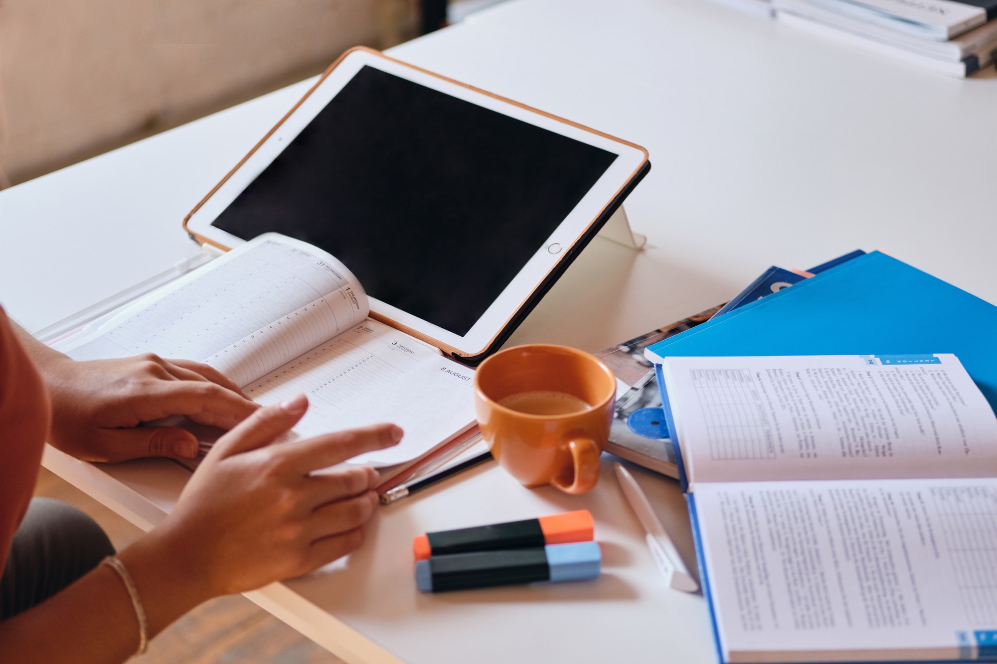 Girl studying with tablet, textbooks and cup of coffee on desk at cozy home