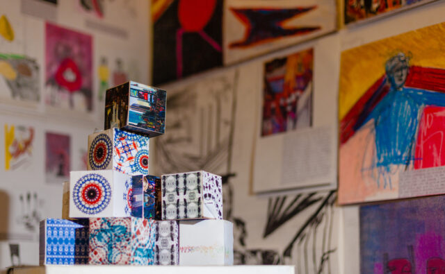 Art project - Decorated boxes stacked in a pyramid shape in front of a blurred background of artwork