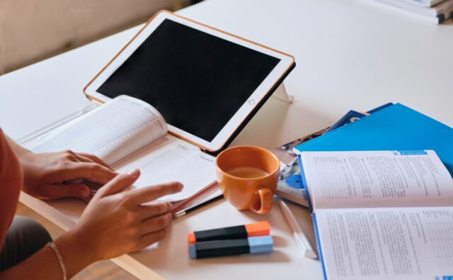 Girl studying with tablet, textbooks and cup of coffee on desk at cozy home