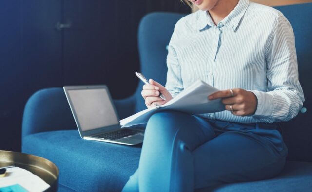 Smiling young businesswoman sitting on a sofa reading documents