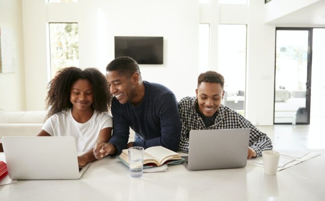 Smiling dad helping his teen kids with their homework, front view, close up